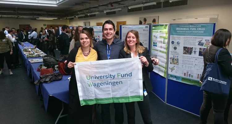 Drie studenten die een vlag met het logo van het University Fund Wageningen ophouden bij een conferentie